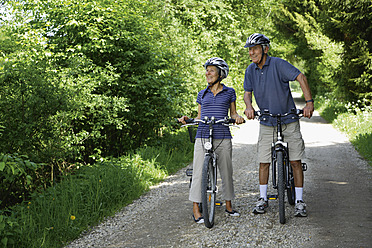 Deutschland, Bayern, Seniorenpaar mit Fahrrad, lächelnd - TCF002634