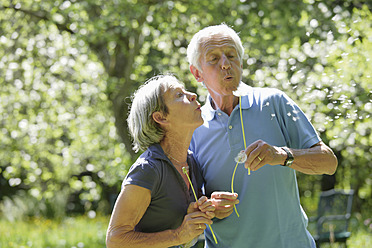 Germany, Bavaria, Senior couple blowing blowball - TCF002638