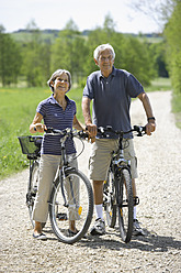 Deutschland, Bayern, Seniorenpaar mit Fahrrad, lächelnd - TCF002642