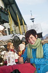 Österreich, Salzburg, Junge Frau mit Tasse, Menschen im Hintergrund - HHF004206