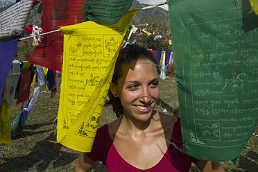 India, Young woman smiling, prayer flags in foreground - MBEF000329