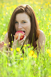 Austria, Young woman lying in field of flowers with apple, portrait - WWF002423