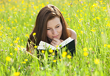 Österreich, Junge Frau mit Buch im Blumenfeld liegend, lächelnd - WWF002422