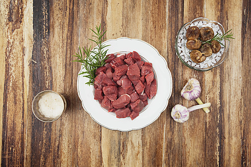 Teller mit rohem Gulasch und getrockneten Feigen, Knoblauchzwiebeln und Bierglas auf Holztisch - GWF001823