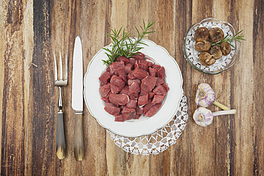 Teller mit rohem Gulasch und getrockneten Feigen und Knoblauchzwiebeln auf einem Holztisch - GWF001824