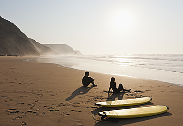 Portugal, Couple sitting on beach by surfboard - MIRF000461