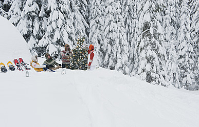 Austria, Salzburg, Men and women sitting by christmas tree in winter - HHF004220