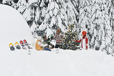 Austria, Salzburg, Men and women sitting by christmas tree in winter - HHF004221