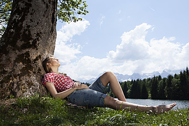 Deutschland, Bayern, Junge Frau liegt im Gras unter einem Baum - RBF000910