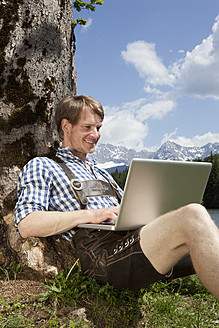 Deutschland, Bayern, Mittlerer erwachsener Mann mit Laptop unter Baum - RBF000931