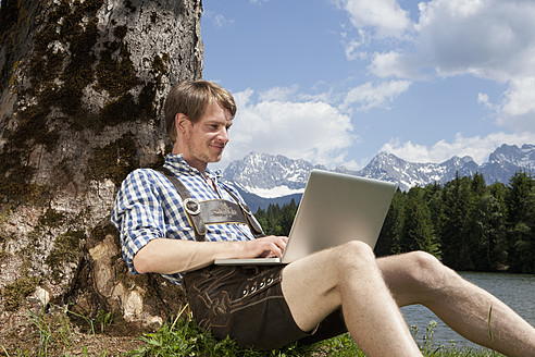 Germany, Bavaria, Mid adult man using laptop under tree - RBF000932