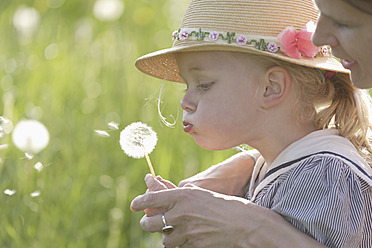 Germany, Bavaria, Mother and daughter blowing dandelion seed head, close up - TCF002792