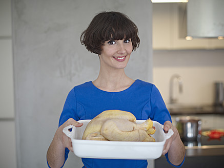 Deutschland, Köln, Junge Frau mit Huhn in Küche, lächelnd, Porträt - RHYF000108