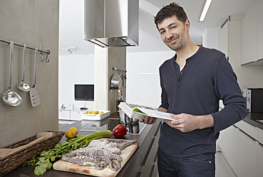 Germany, Cologne, Mid adult man with cook book in kitchen, portrait - RHYF000112