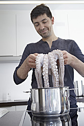 Deutschland, Köln, Mittlerer Erwachsener Mann kocht Tintenfisch in Küche, lächelnd - RHYF000117