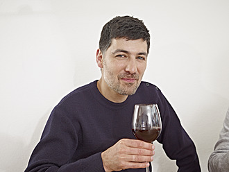 Deutschland, Köln, Mittlerer erwachsener Mann trinkt Wein in Küche, lächelnd - RHYF000175