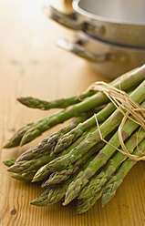 Bundle of green asparagus in front of pans on table - KSWF000897