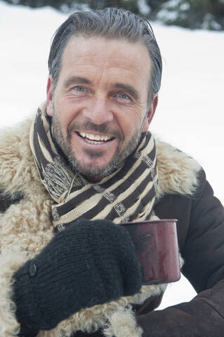 Österreich, Land Salzburg, Älterer Mann mit Teetasse im Schnee, lächelnd, Porträt, lizenzfreies Stockfoto