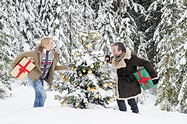 Österreich, Land Salzburg, Paar hält Weihnachtsgeschenk im Schnee, lächelnd - HHF004263