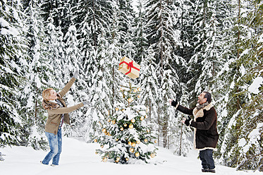 Austria, Salzburg County, Couple playing with christmas gift in snow, smiling - HHF004264