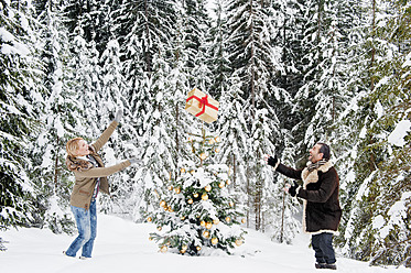 Österreich, Salzburger Land, Pärchen spielt mit Weihnachtsgeschenk im Schnee, lächelnd - HHF004264