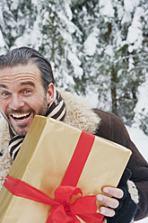 Austria, Salzburg County, Mature man standing with christmas parcel, smiling, portrait - HHF004266