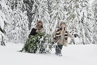 Austria, Salzburg County, Couple pulling christmas tree in winter landscape - HHF004290