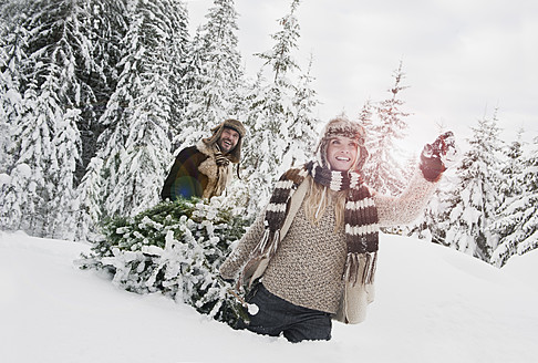 Austria, Salzburg County, Couple pulling christmas tree in winter landscape - HHF004291