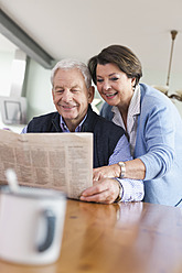 Germany, Leipzig, Senior man and woman reading newspaper, smiling - WESTF018740