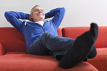 Deutschland, Leipzig, Älterer Mann entspannt sich auf der Couch, lächelnd - WESTF018777