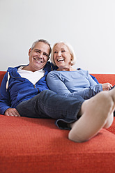 Germany, Leipzig, Senior man and woman relaxing on couch, smiling - WESTF018779