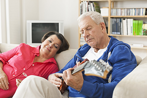 Deutschland, Leipzig, Älterer Mann spielt E-Gitarre auf Sofa, Frau sitzt daneben - WESTF018881