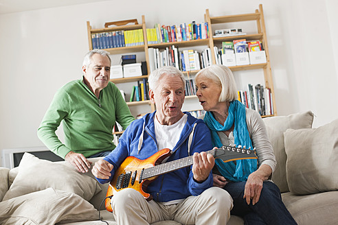 Deutschland, Leipzig, Älterer Mann spielt E-Gitarre, Mann und Frau sitzen daneben - WESTF018883
