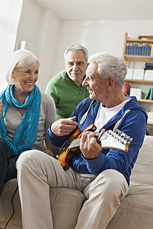 Deutschland, Leipzig, Älterer Mann spielt E-Gitarre, Mann und Frau sitzen daneben - WESTF018884