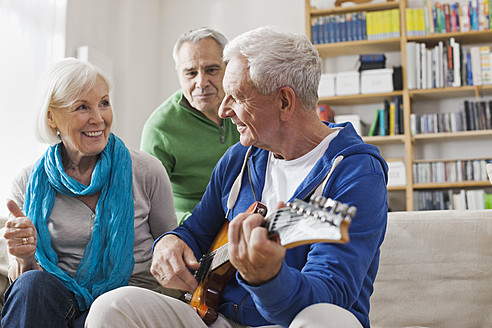 Deutschland, Leipzig, Älterer Mann spielt E-Gitarre, Mann und Frau sitzen daneben - WESTF018885