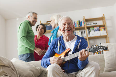 Deutschland, Leipzig, älterer Mann spielt E-Gitarre, Mann und Frau im Hintergrund, lizenzfreies Stockfoto