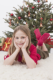 Mädchen auf Pelzteppich liegend, Weihnachtsbaum und Geschenke im Hintergrund - BMYF000331