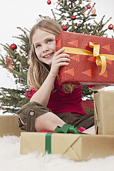 Mädchen sitzt auf Teppich mit Geschenken, Weihnachtsbaum im Hintergrund - BMYF000334