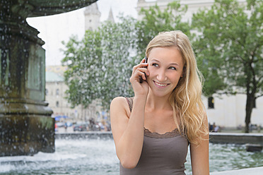 Deutschland, Bayern, München, Junge Frau telefoniert vor der Ludwig-Maximilians-Universität, lächelnd - TCF002801