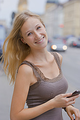 Deutschland, Bayern, München, Junge Frau mit Smartphone vor der Bayerischen Staatsbibliothek in der Ludwigstraße - TCF002814