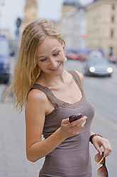 Deutschland, Bayern, München, Junge Frau mit Smartphone vor der Bayerischen Staatsbibliothek in der Ludwigstraße - TCF002815