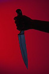 Human hand holding kitchen knife against red background - FLF000107