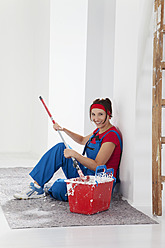 Germany, Bavaria, Young woman sitting with paint tin and paint brush, smiling, portrait - MAEF004751