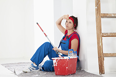 Germany, Bavaria, Young woman tired, sitting with paint tin and brush - MAEF004752