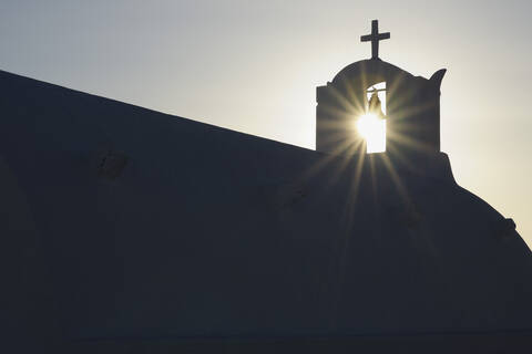 Griechenland, Die Sonne scheint durch den Glockenturm im Dorf Oia auf Santorin, lizenzfreies Stockfoto