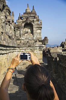 Indonesien, Junge Frau fotografiert Buddha-Statue im Borobudur-Tempel - MBEF000410