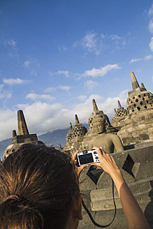 Indonesien, Junge Frau fotografiert Buddha-Statue im Borobudur-Tempel - MBEF000408