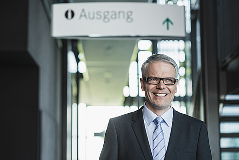 Germany, Stuttgart, Businessman standing in office building, smiling - MFPF000194
