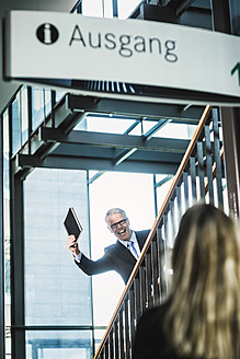 Germany, Stuttgart, Businessman showing diary to woman on stairs of office building - MFPF000200