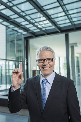 Deutschland, Stuttgart, Geschäftsmann mit einem Finger, lächelnd, Porträt, lizenzfreies Stockfoto